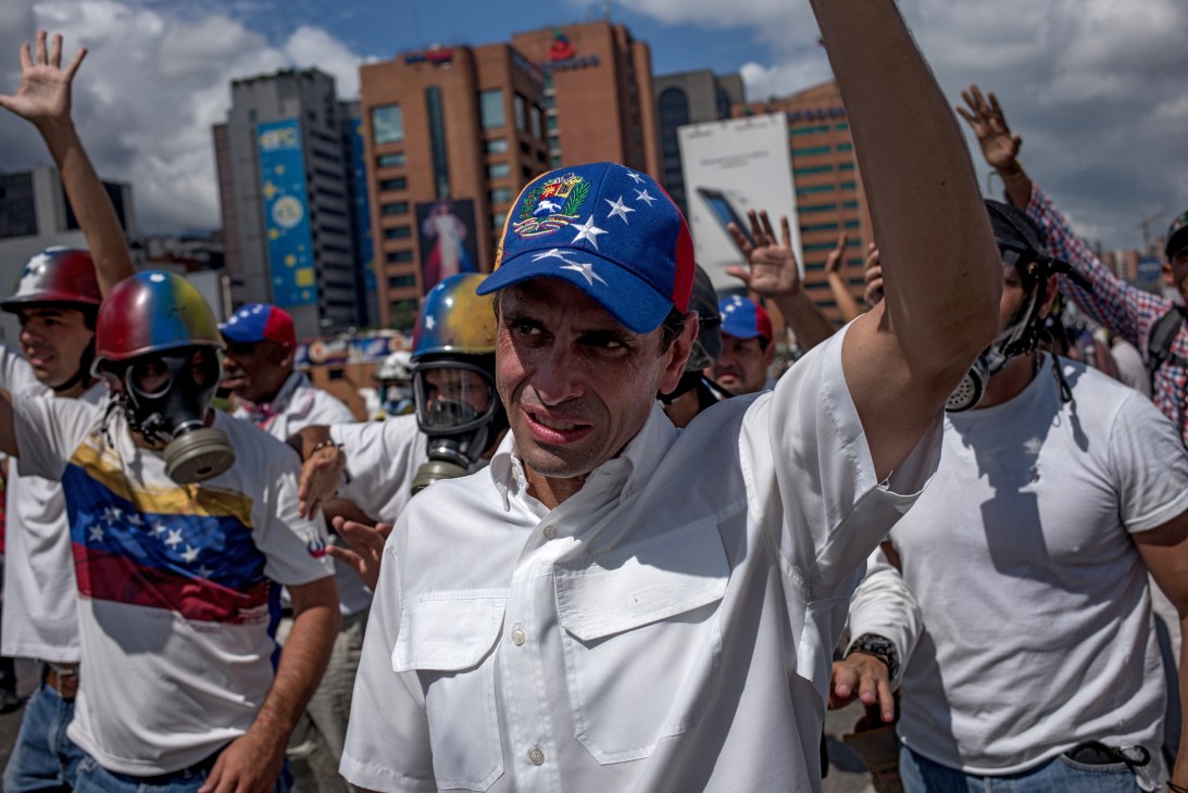 Henrique Capriles wearing Venezuelan flag cap raises hand at protest with supporters in white shirts