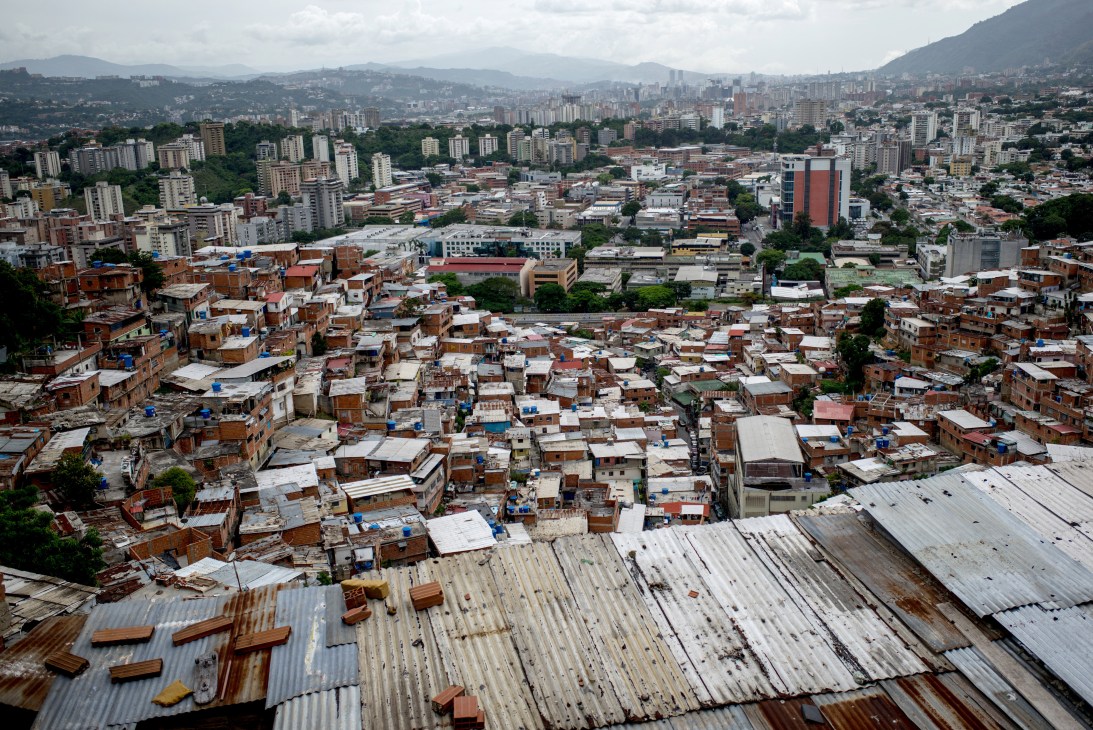 Aerial view of densely packed informal settlements with corrugated metal roofs in foreground and modern city buildings