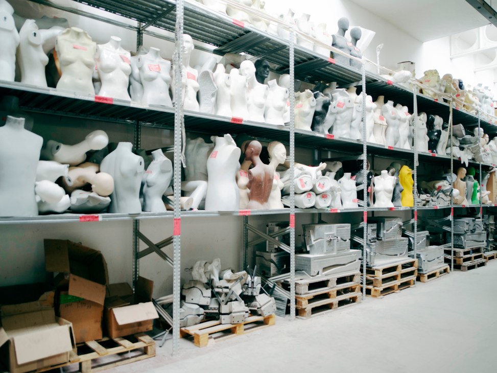 Industrial shelving units stacked with white mannequin torsos, heads, and body parts in La Rosa's warehouse.