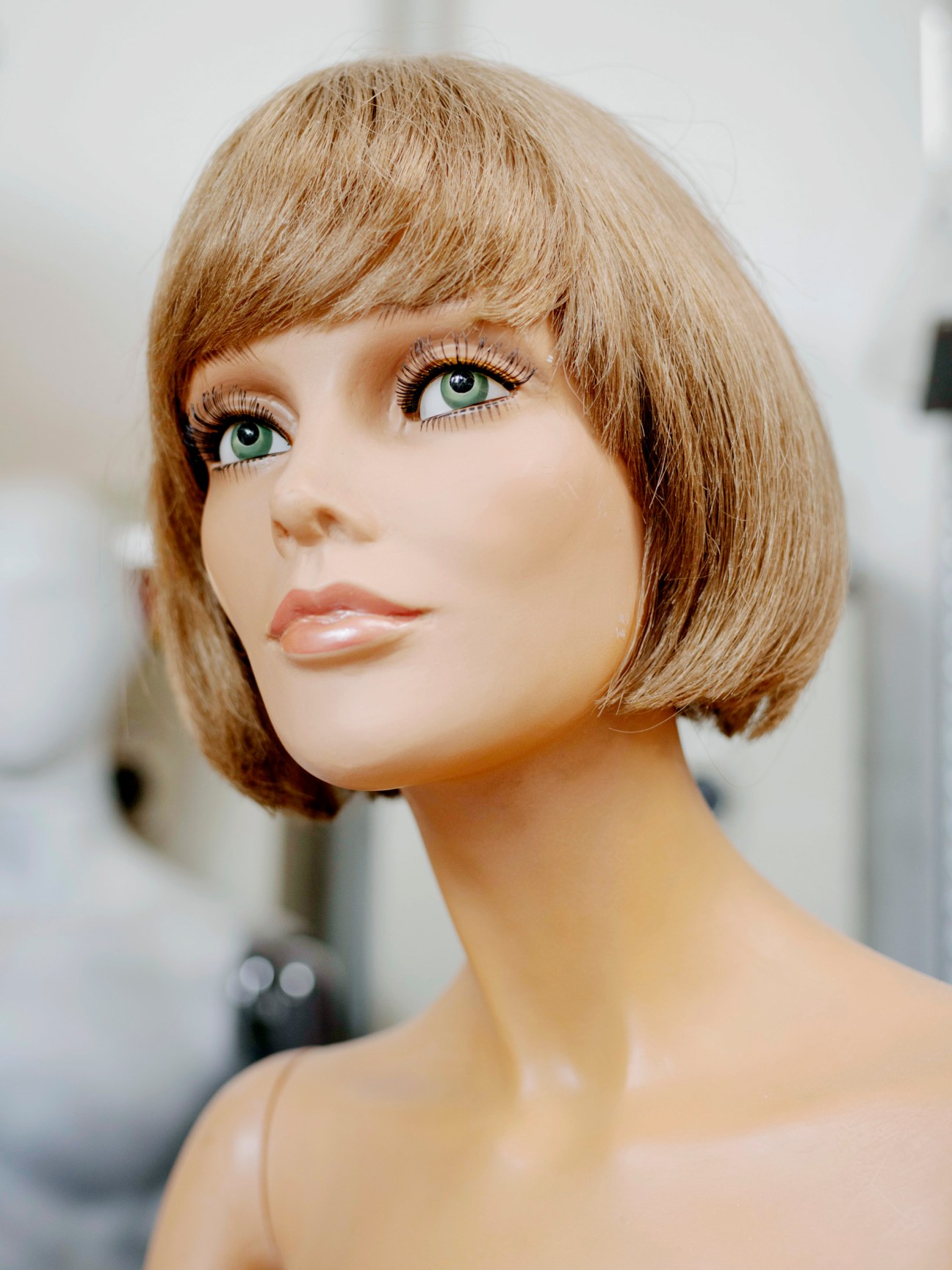 La Rosa mannequin head with blonde bob haircut, green eyes and painted facial features in profile.