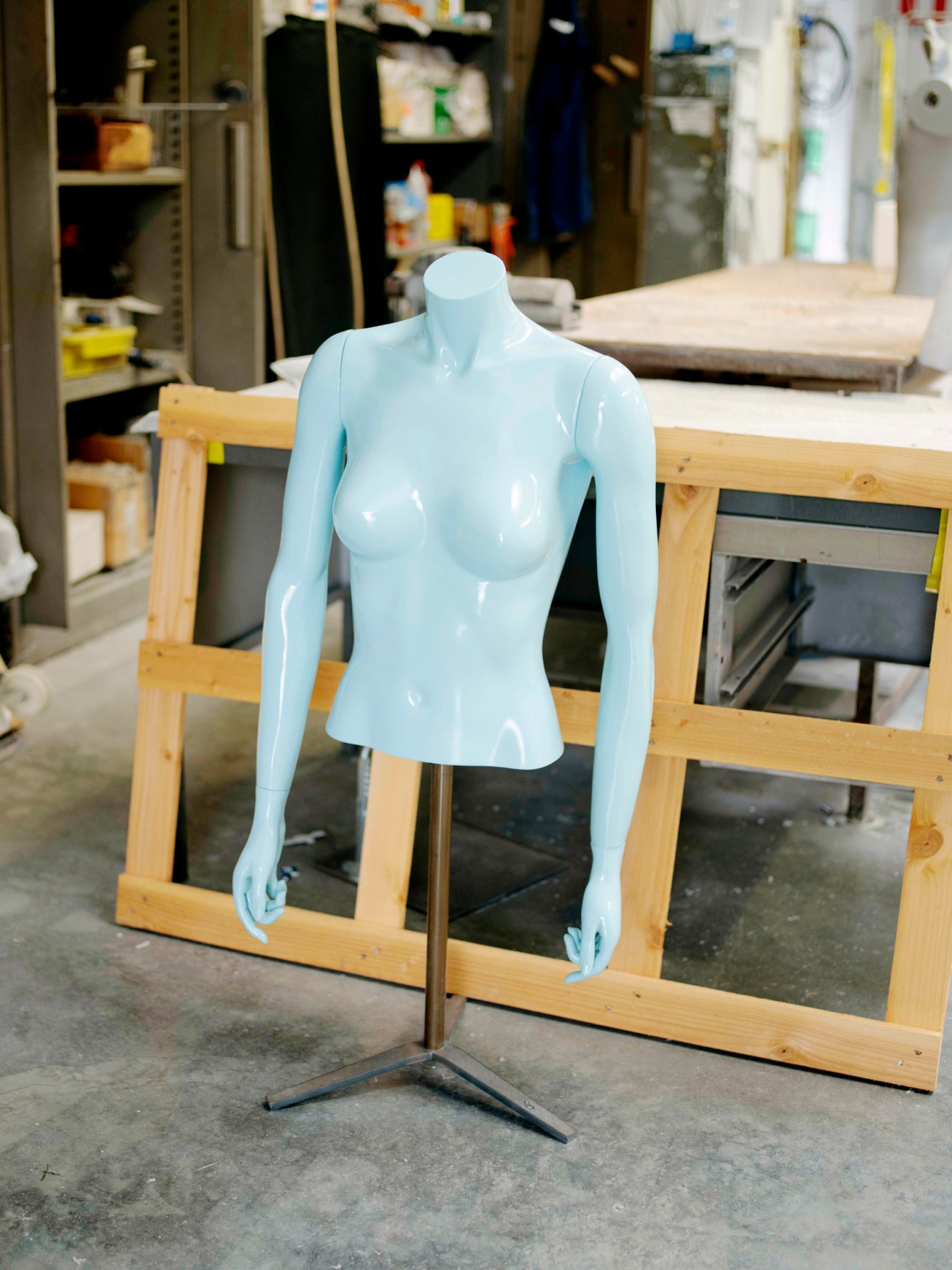 Light blue glossy mannequin torso displayed on wooden stand in La Rosa factory workshop.