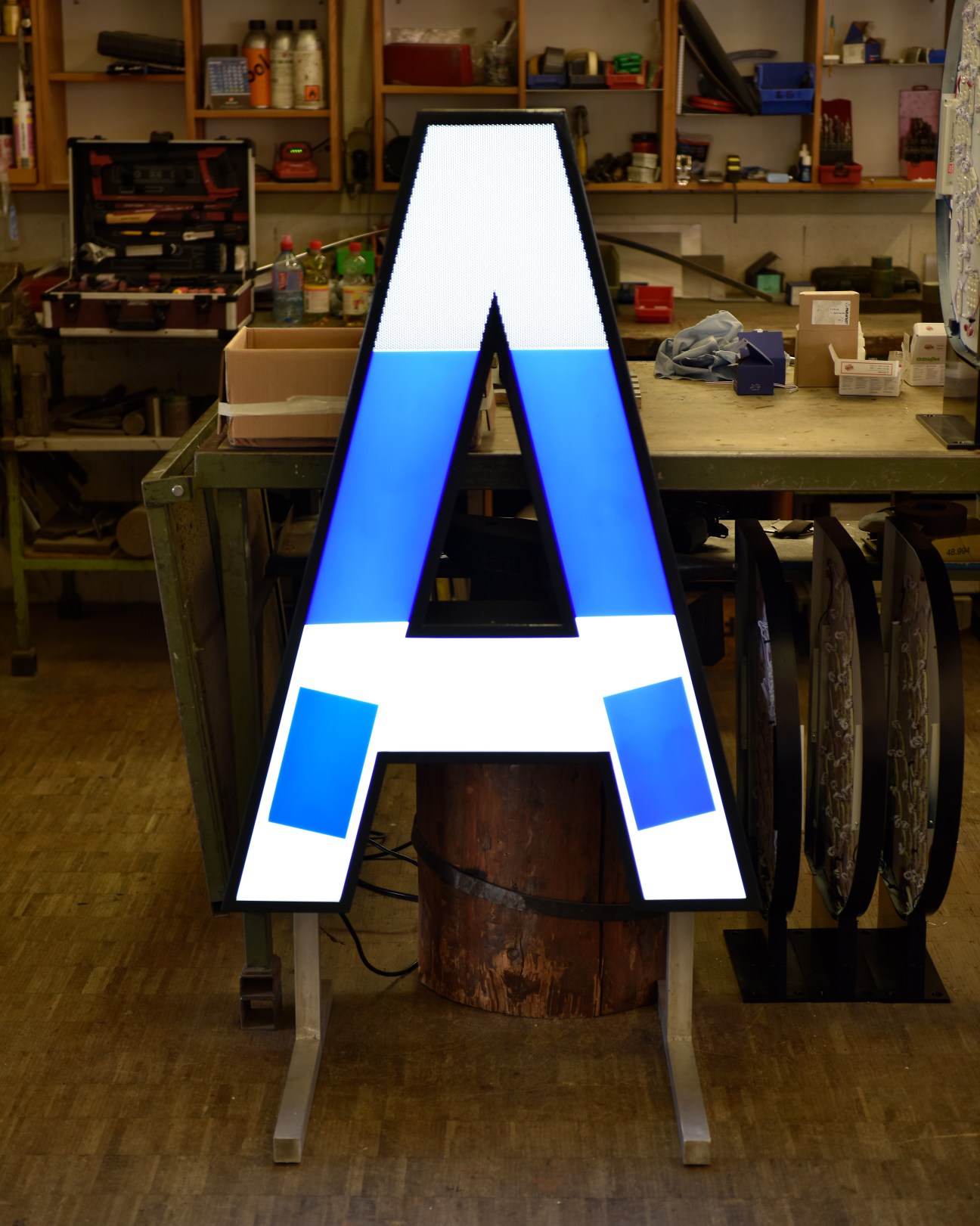 Large illuminated letter A with blue and white sections displayed in a workshop setting