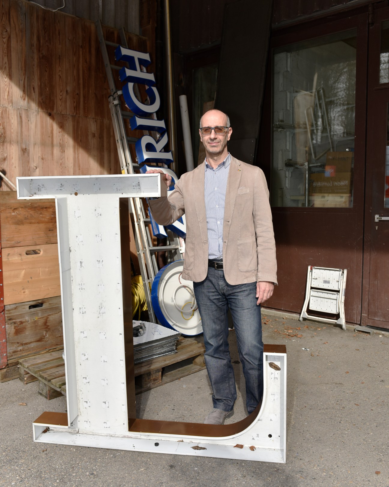 Tony Santangelo standing next to a large white metal letter frame in his neon sign workshop