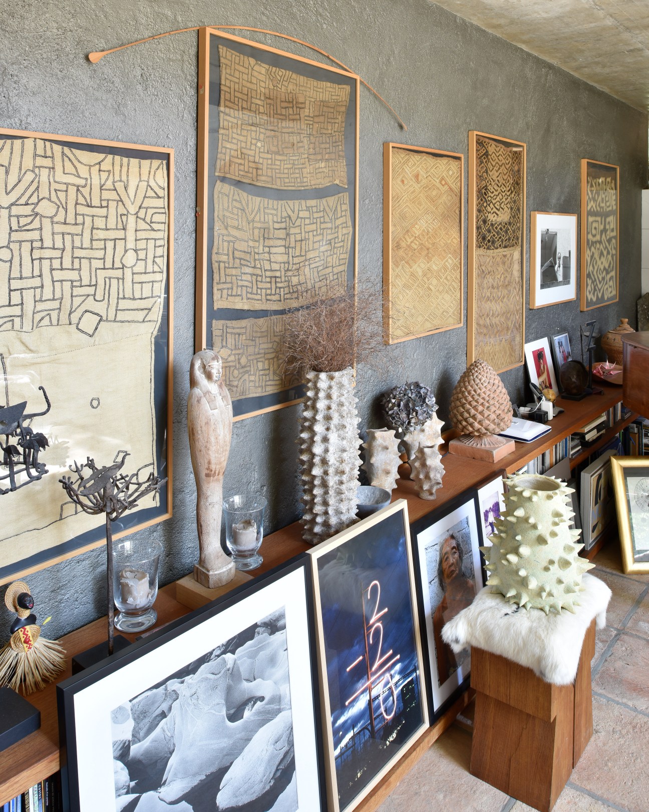 Living room wall displaying African textiles in wooden frames and decorative sculptural objects on a wooden shelf.