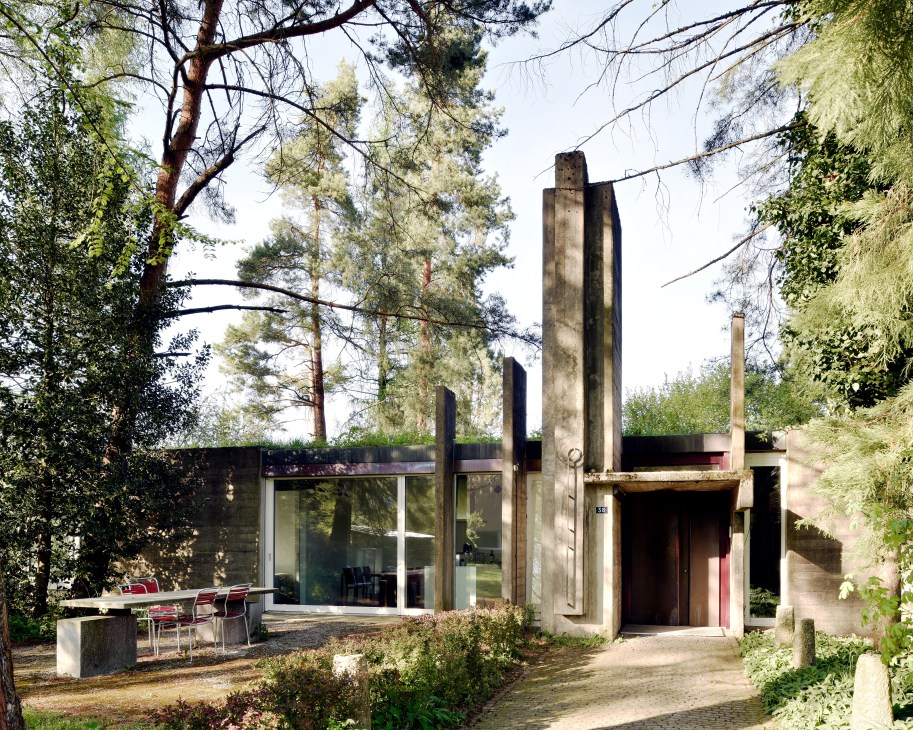Modernist concrete architecture studio with tall vertical pillars surrounded by pine and birch trees.