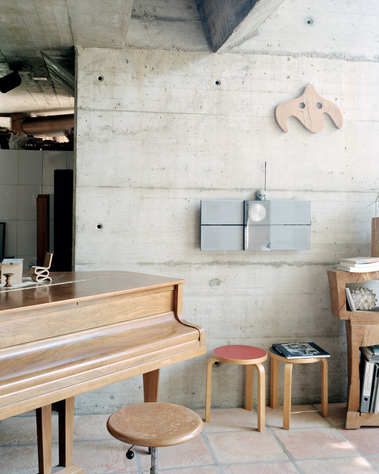 Minimalist interior with exposed concrete wall, wooden piano, Hans Arp sculpture, and mid-century furniture.