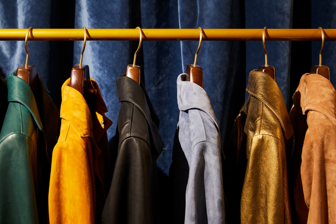 Colorful leather jackets hanging on a brass rail against a dark blue curtain backdrop.