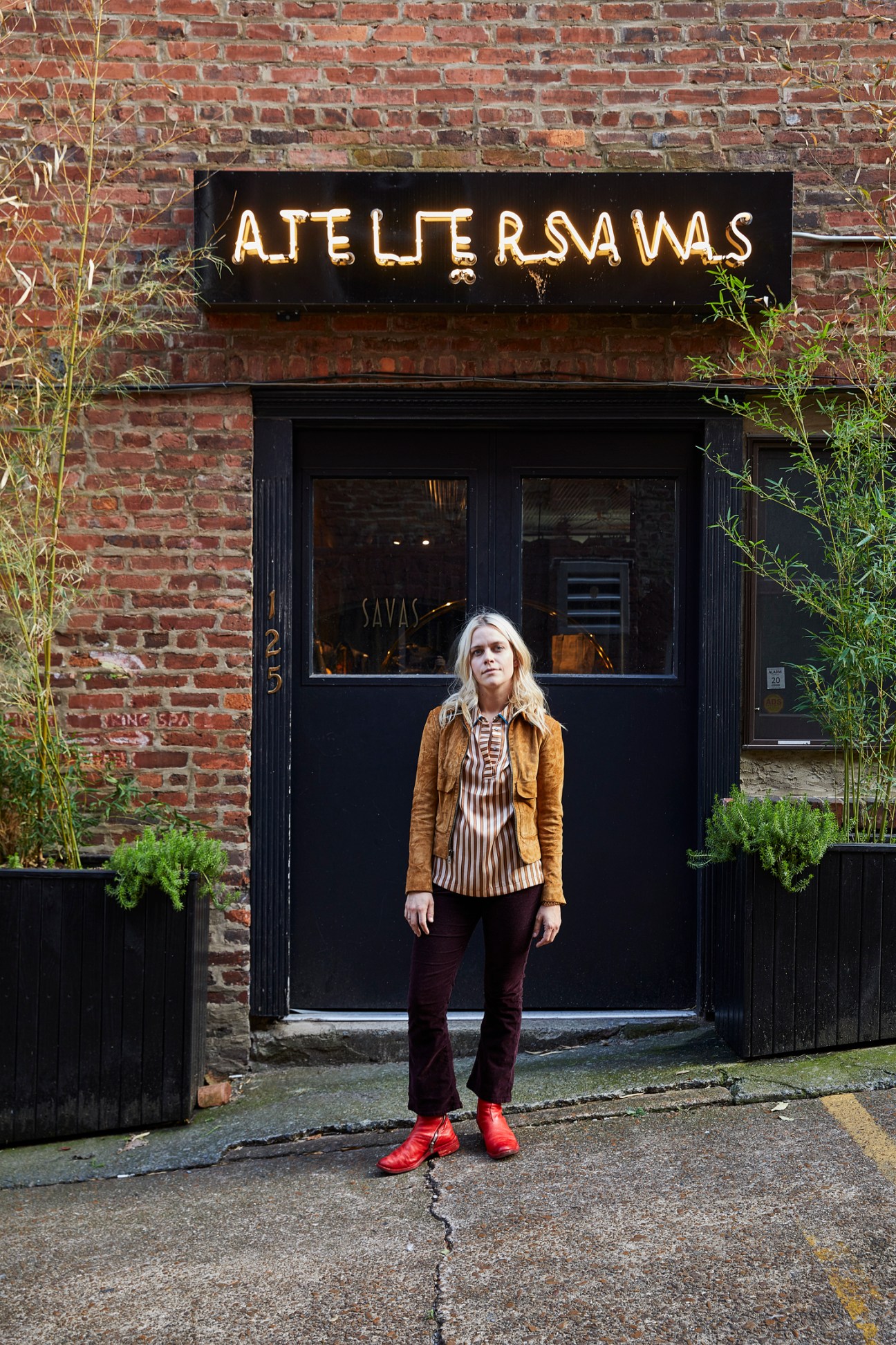 Savannah Yarborough of Savas stands in front of her storefront with neon sign on brick wall in Nashville.