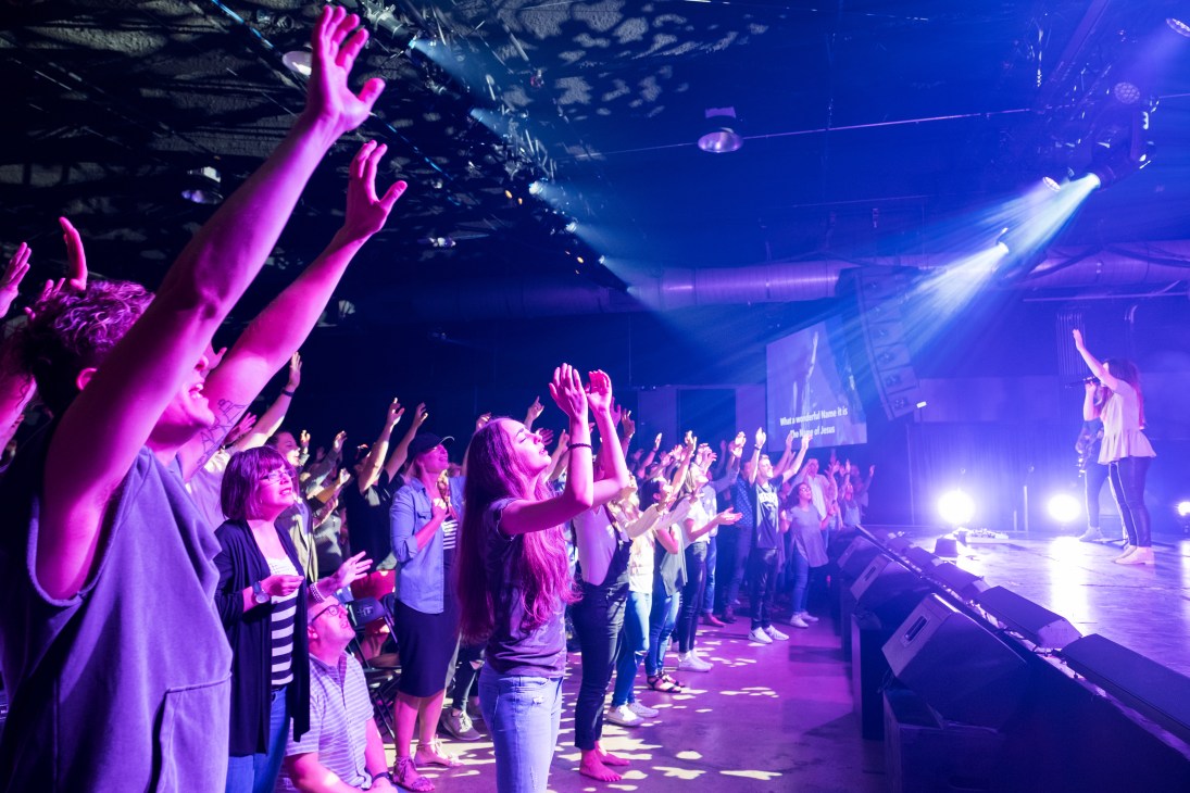 Cody Carnes performing on stage at The Belonging Co church service in Nashville with audience members raising their hands in worship.