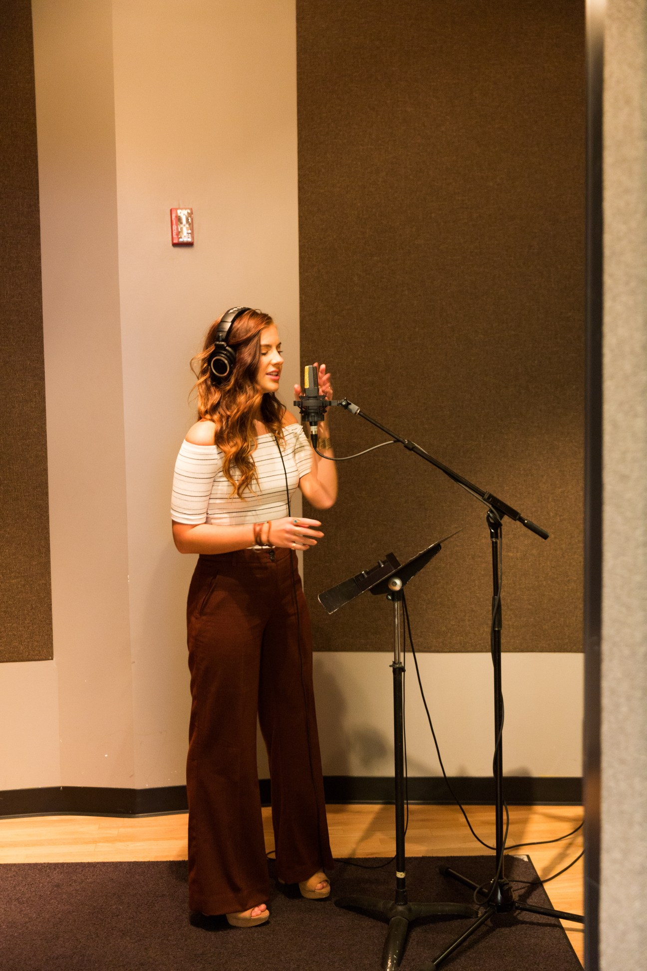 Riley Clemmons recording in a studio while wearing headphones at a microphone.