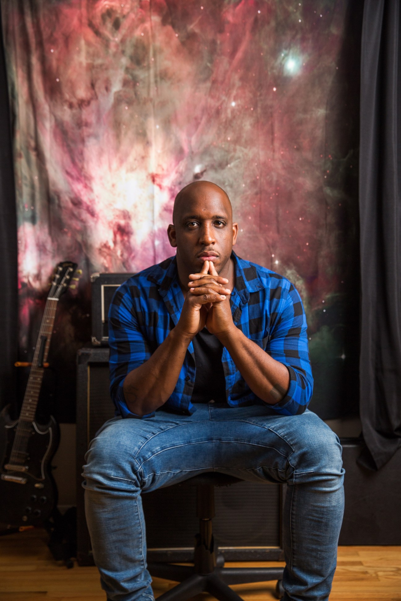 Christian rapper Derek Minor sitting in his Nashville studio with a guitar and cosmic backdrop.