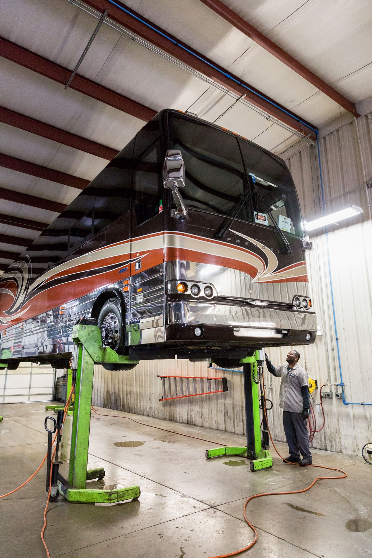 A tour bus lifted on a green hydraulic platform for maintenance in an industrial warehouse.