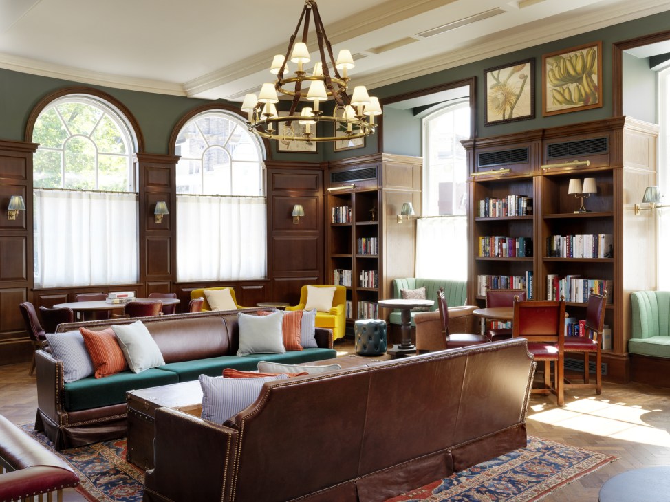 Hotel library at University Arms Cambridge with leather seating, wooden bookshelves, arched windows and chandelier.