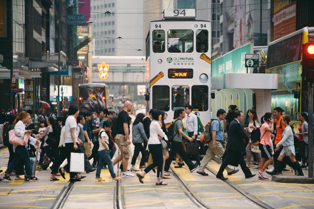 Crowded Hong Kong street with a white Old Mutual tram numbered 94 carrying passengers through busy urban intersection.