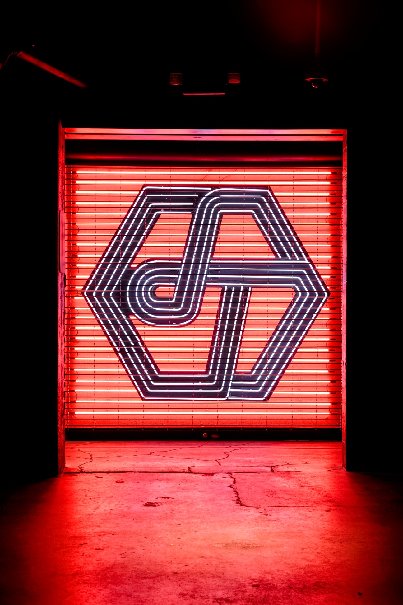 Red neon-lit roller shutter door with geometric logo design in dark urban setting