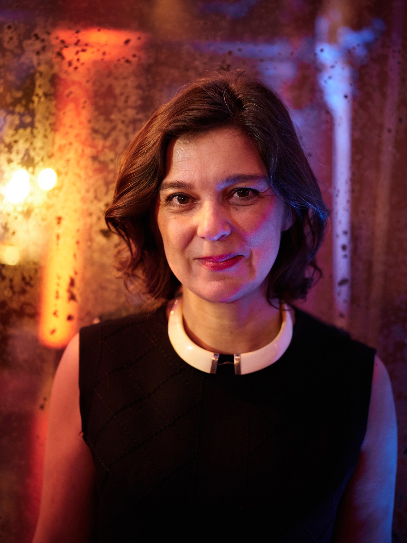 Florence Martin-Kessler, founder of Live Magazine, poses against a weathered textured wall with warm and cool atmospheric lighting.