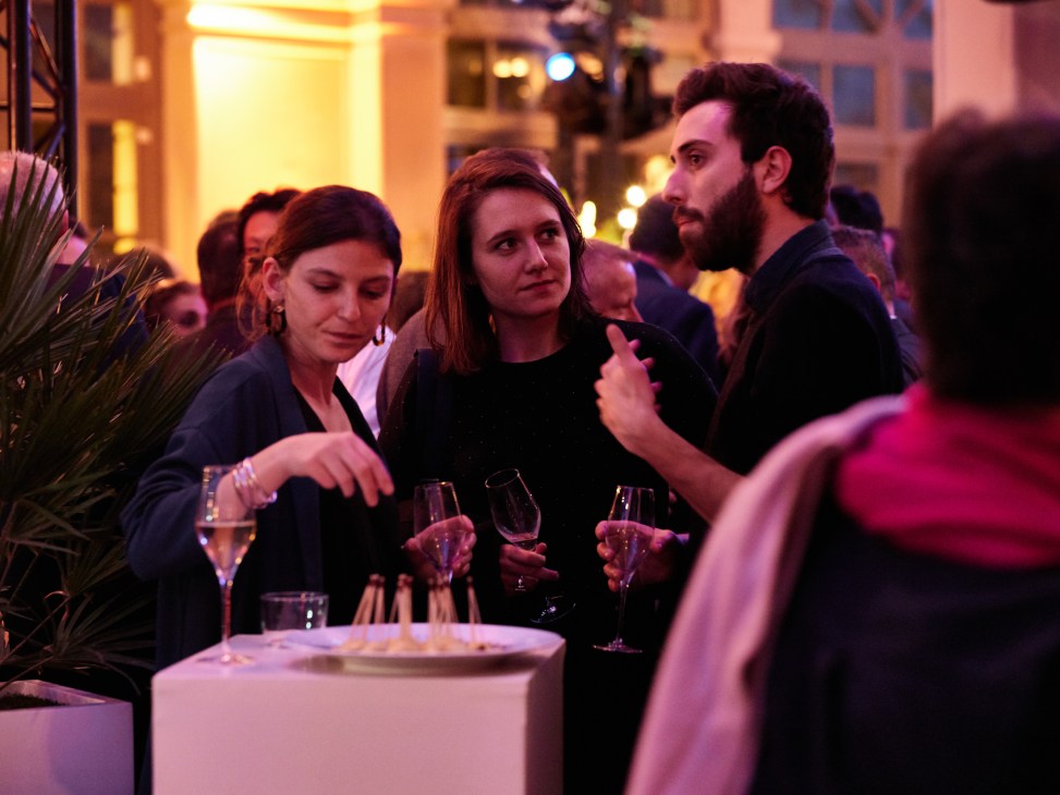 Guests holding wine glasses and conversing at a social gathering after a Live Magazine show.