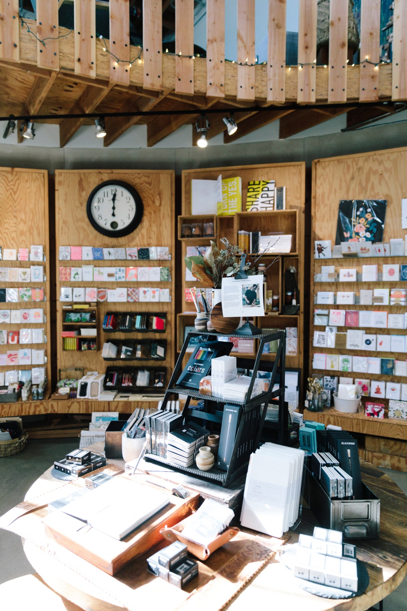 Interior of a modern stationery shop with wooden shelving displaying art supplies, books, and decorative items.