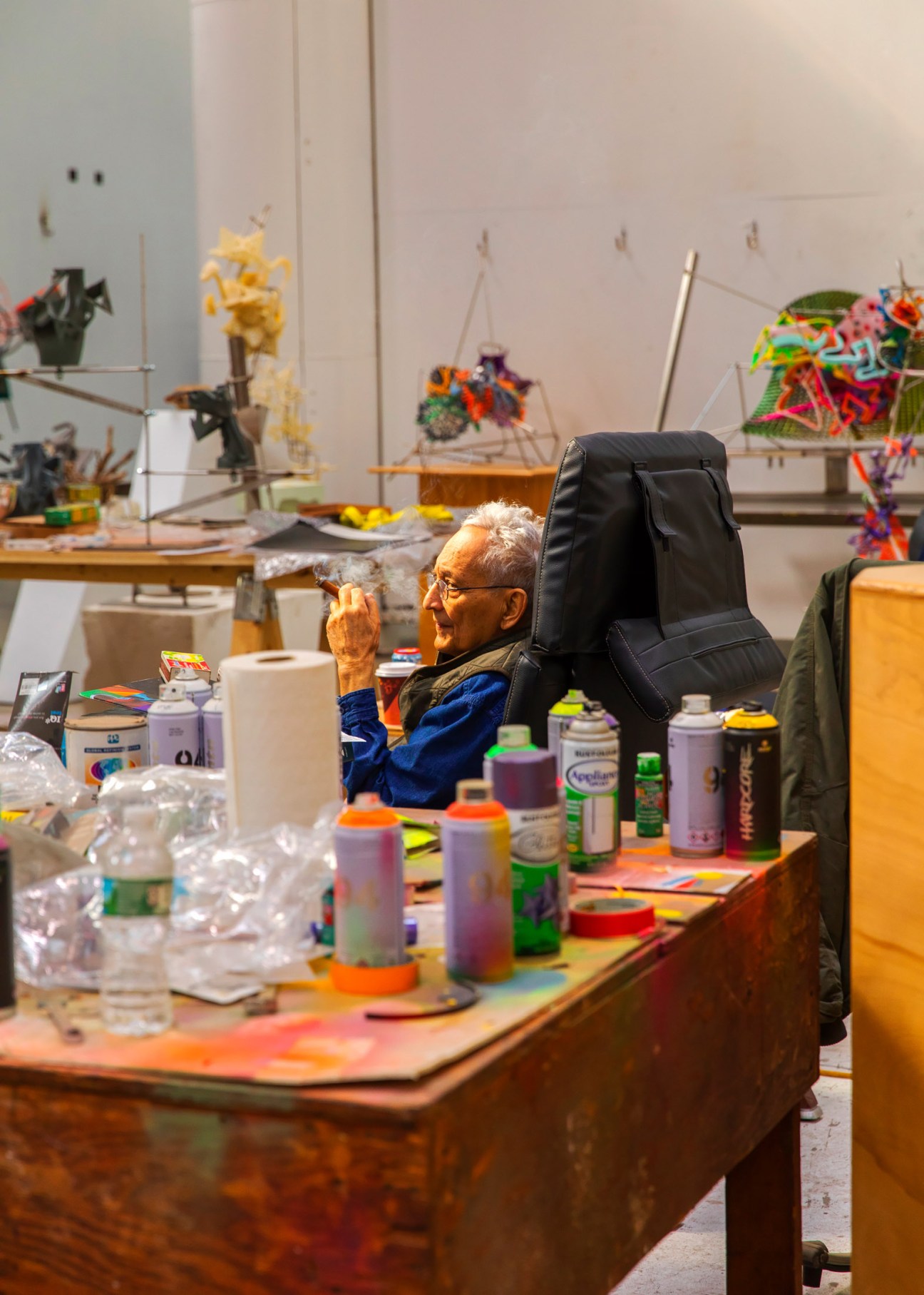 Artist Frank Stella seated in his studio surrounded by colorful art materials and sculptural works.