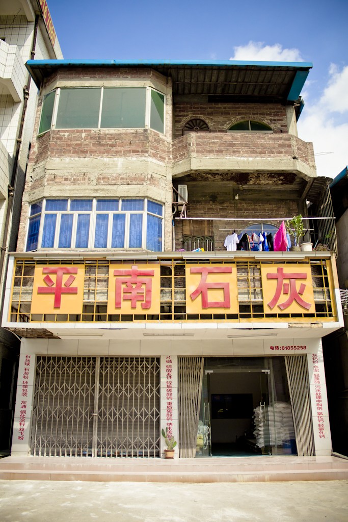 A weathered residential building in Chashan factory town with blue-roofed upper levels and Chinese signage on yellow storefront below.