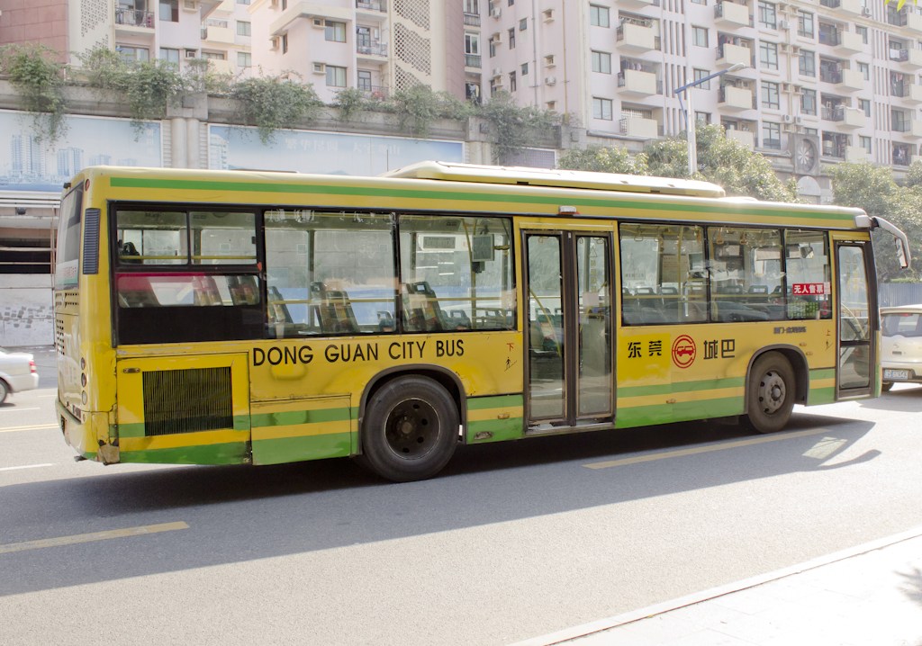 A yellow and green Dongguan city bus parked on a street with apartment buildings in the background.