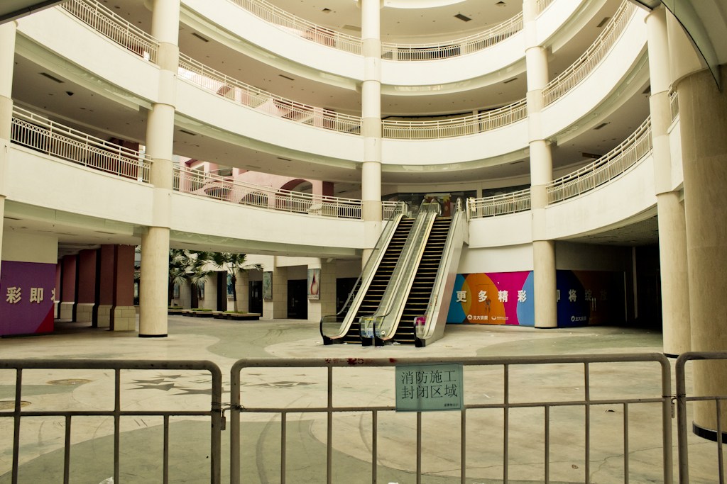 Empty shopping mall gallery with still escalators and closed storefronts in New South China Mall.