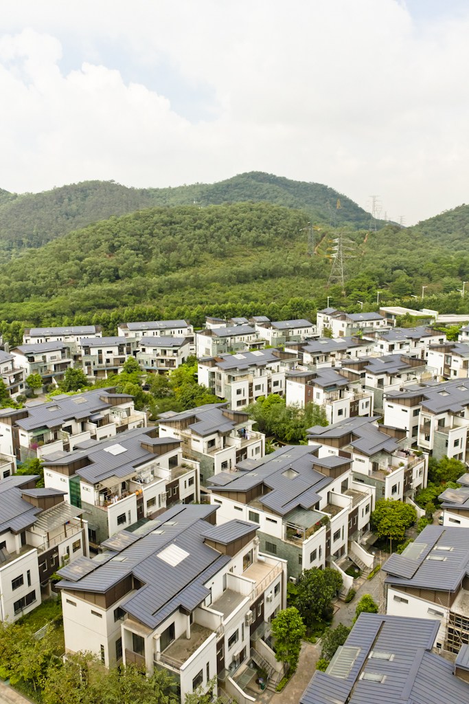 Aerial view of residential buildings with dark roofs in Dynatown, Dongguan, with forested hills in the background.