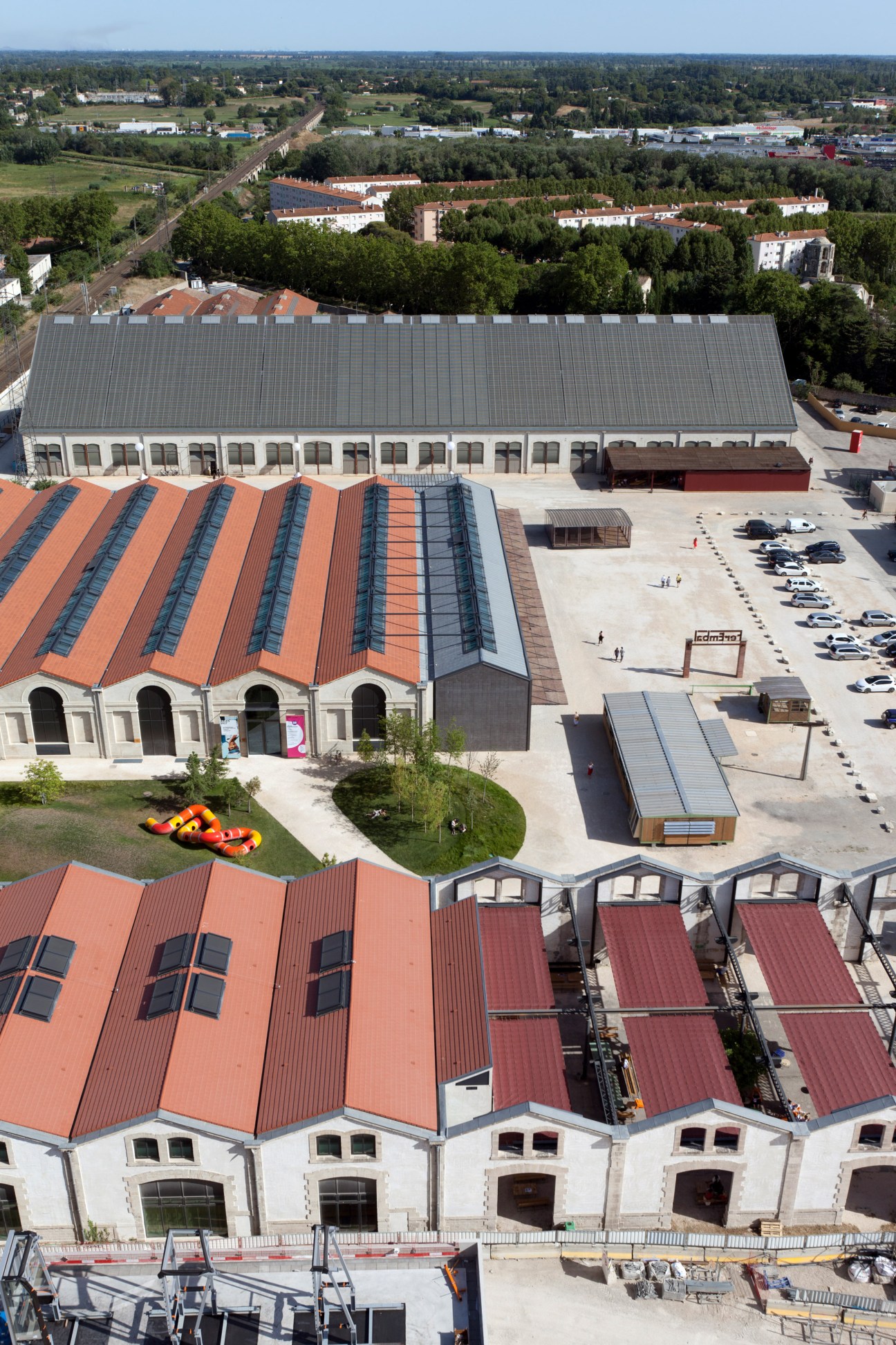 Aerial view of converted railway warehouses with red tile roofs, parking areas and surrounding residential buildings