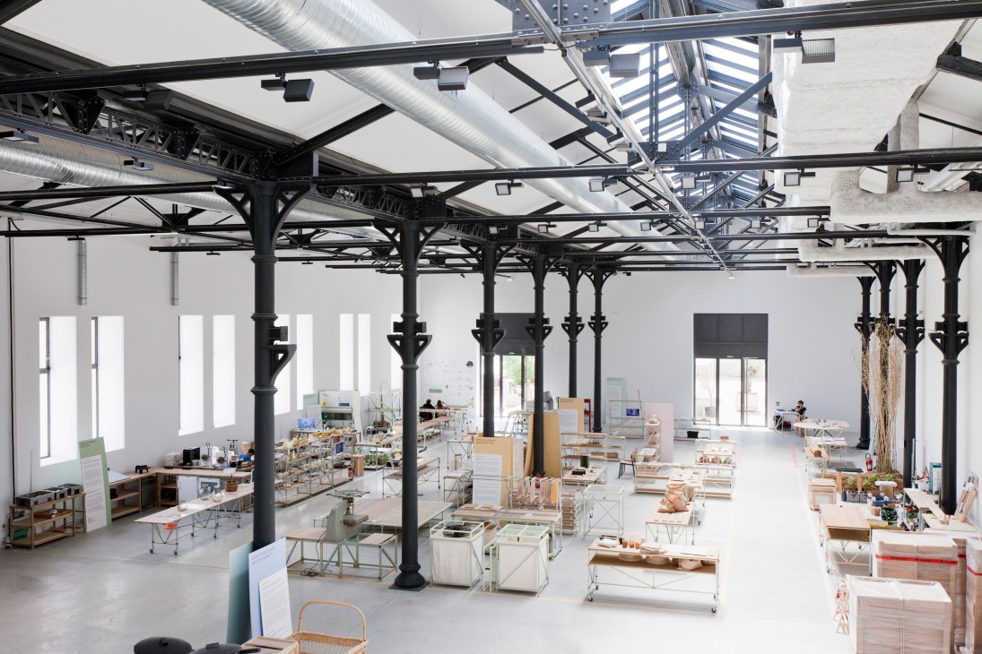 Large industrial workspace with exposed black columns, white walls, and scattered work tables and equipment throughout