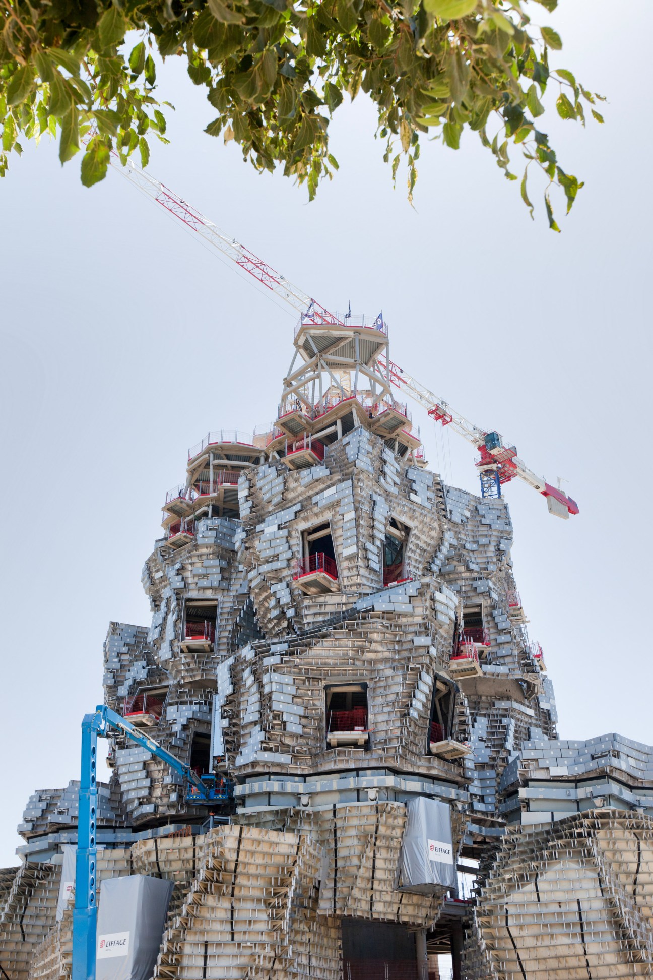 Gehry's tower under construction with metallic facade, scaffolding, and construction cranes
