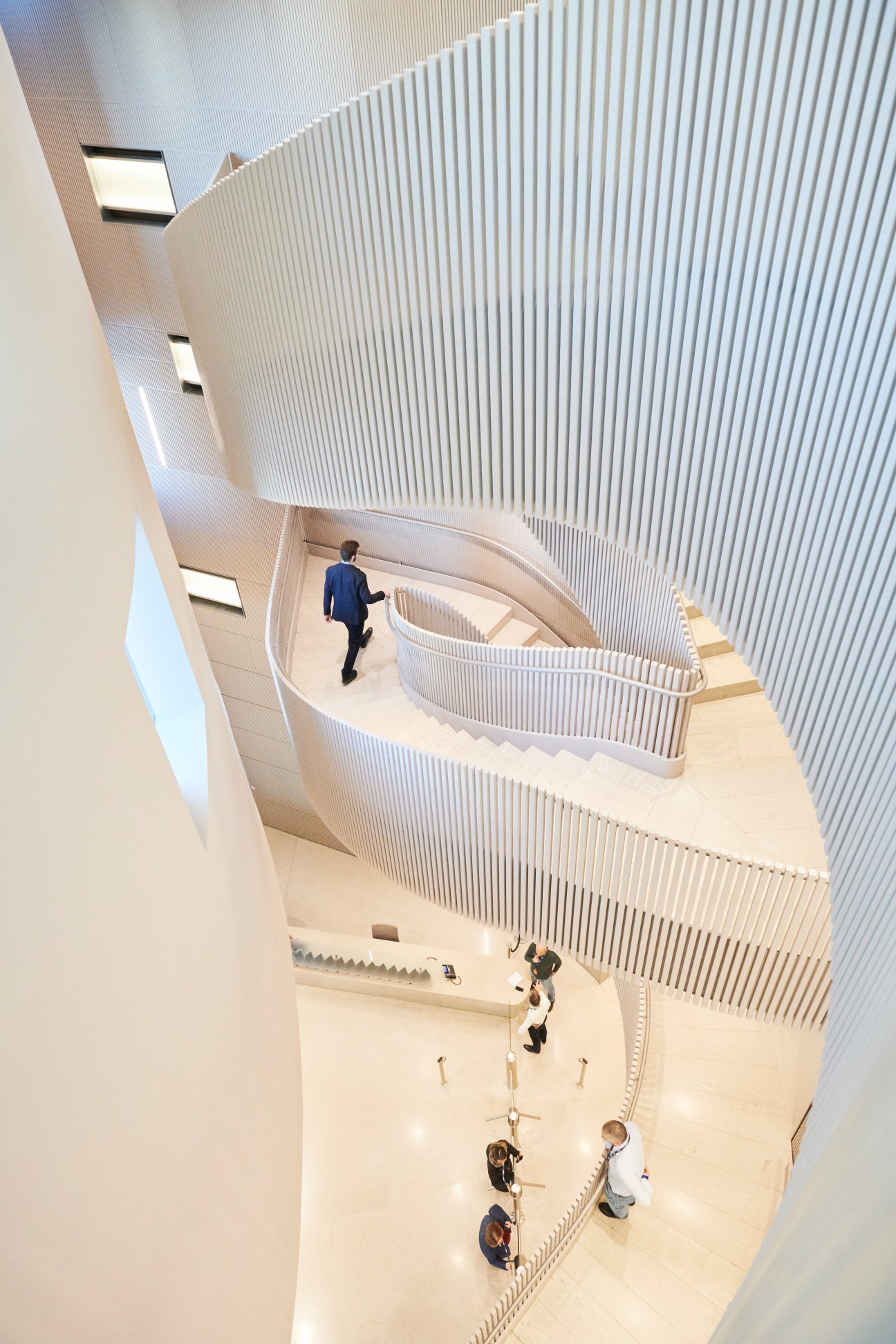 Modern sculptural staircase with white vertical slats and curved limestone steps in office building interior