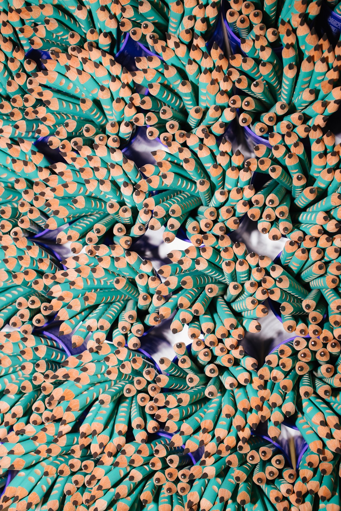 Overhead view of turquoise and natural wood-colored pencils with sharpened tips arranged closely together.