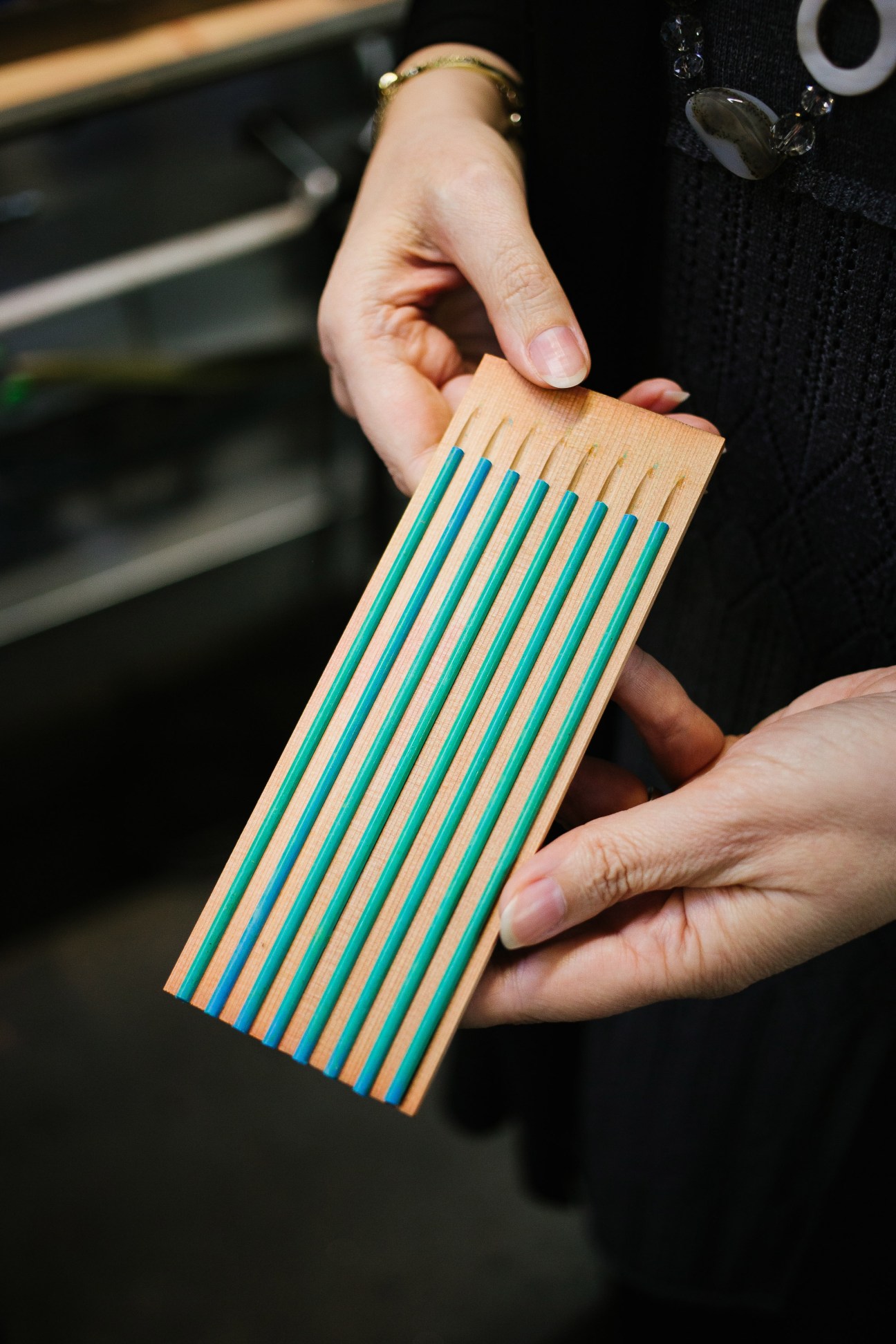 Person holding wooden pencil slats with turquoise and natural wood striped pattern.