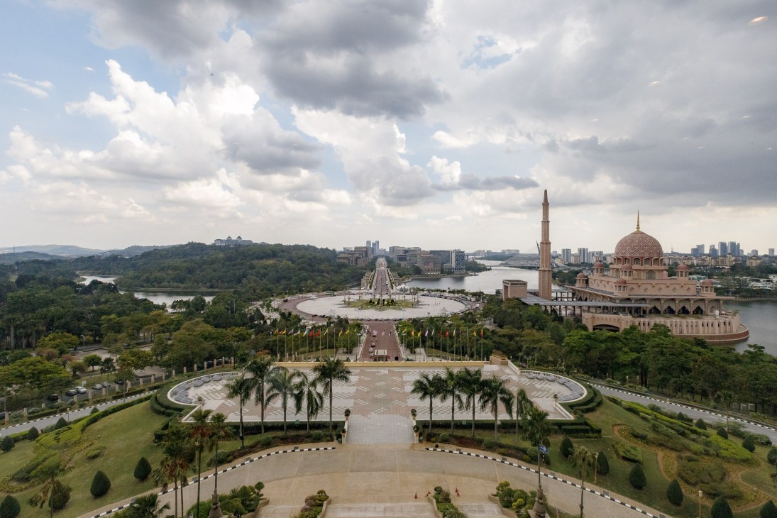 Aerial view of Putrajaya's government district with mosque, circular plaza, palm trees and river.
