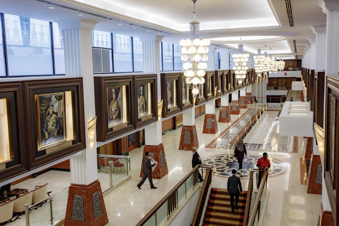 Interior of Malaysian parliament with portraits of kings and prime ministers displayed in illuminated frames along the walls.