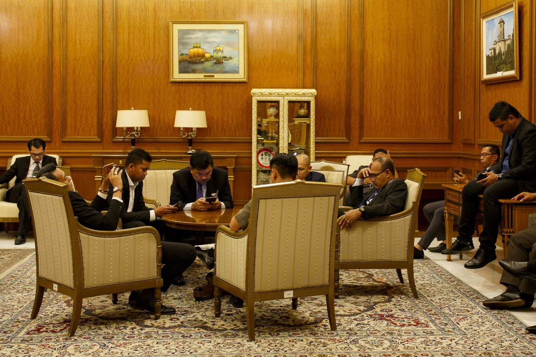 Security officers stand outside a formal government meeting room with wood paneling and upholstered chairs.
