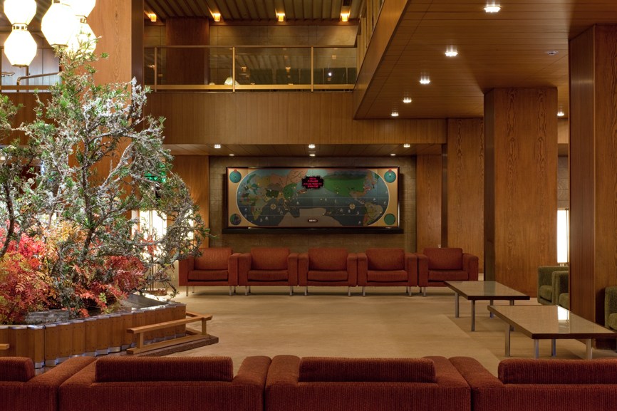 Hotel Okura's 1960s lobby featuring a Seiko world clock, wooden paneling, red seating, and seasonal floral arrangement.