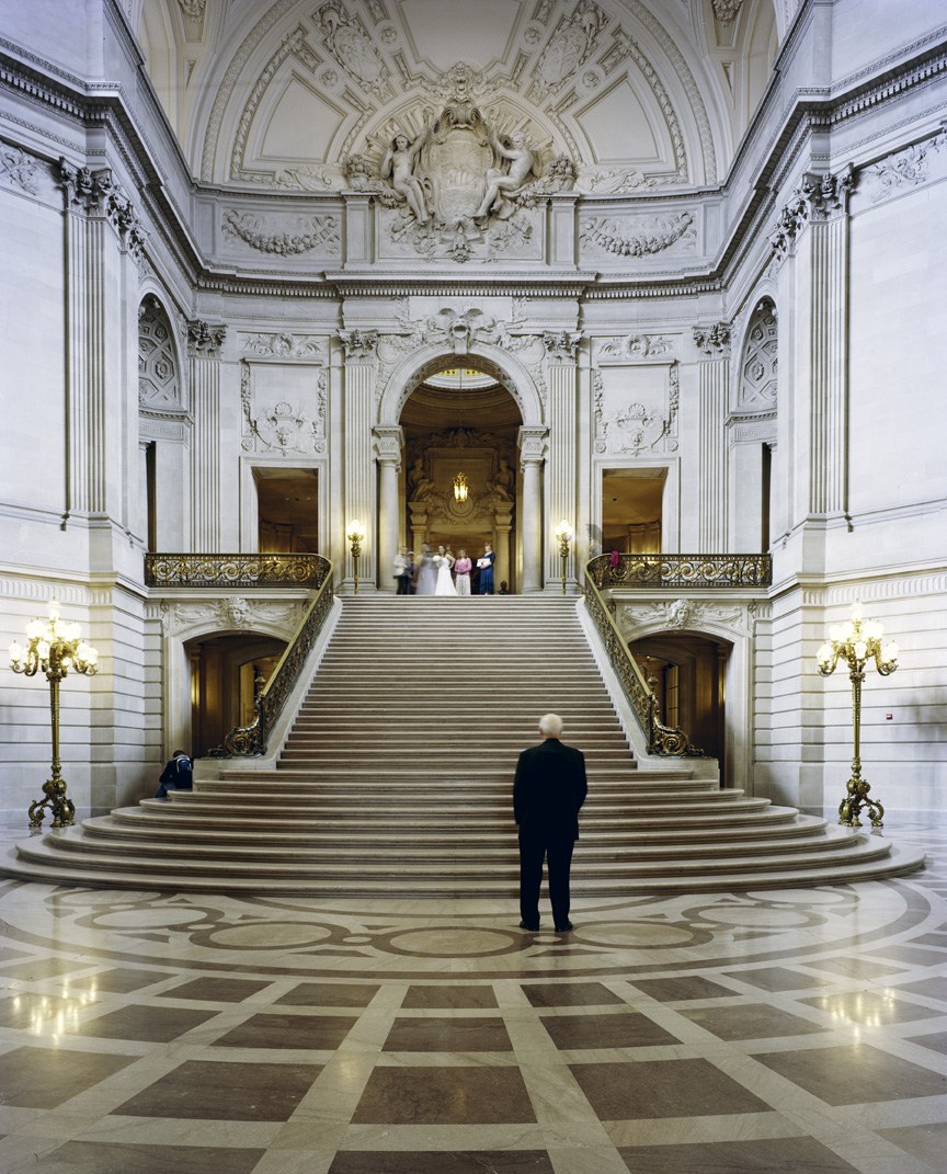 Interior of San Francisco City Hall with grand staircase, ornate ceiling, and classical columns.