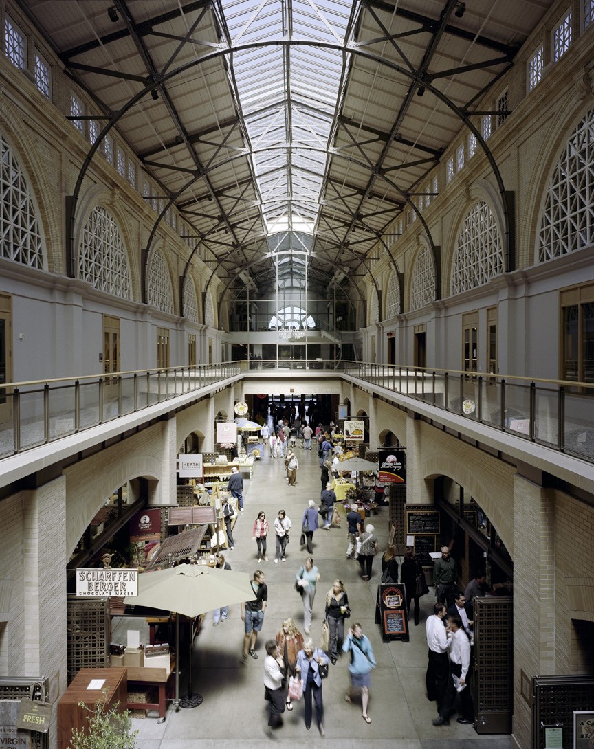 Interior view of San Francisco Ferry Terminal with vaulted glass ceiling, two levels of shops and vendors, and people browsing.