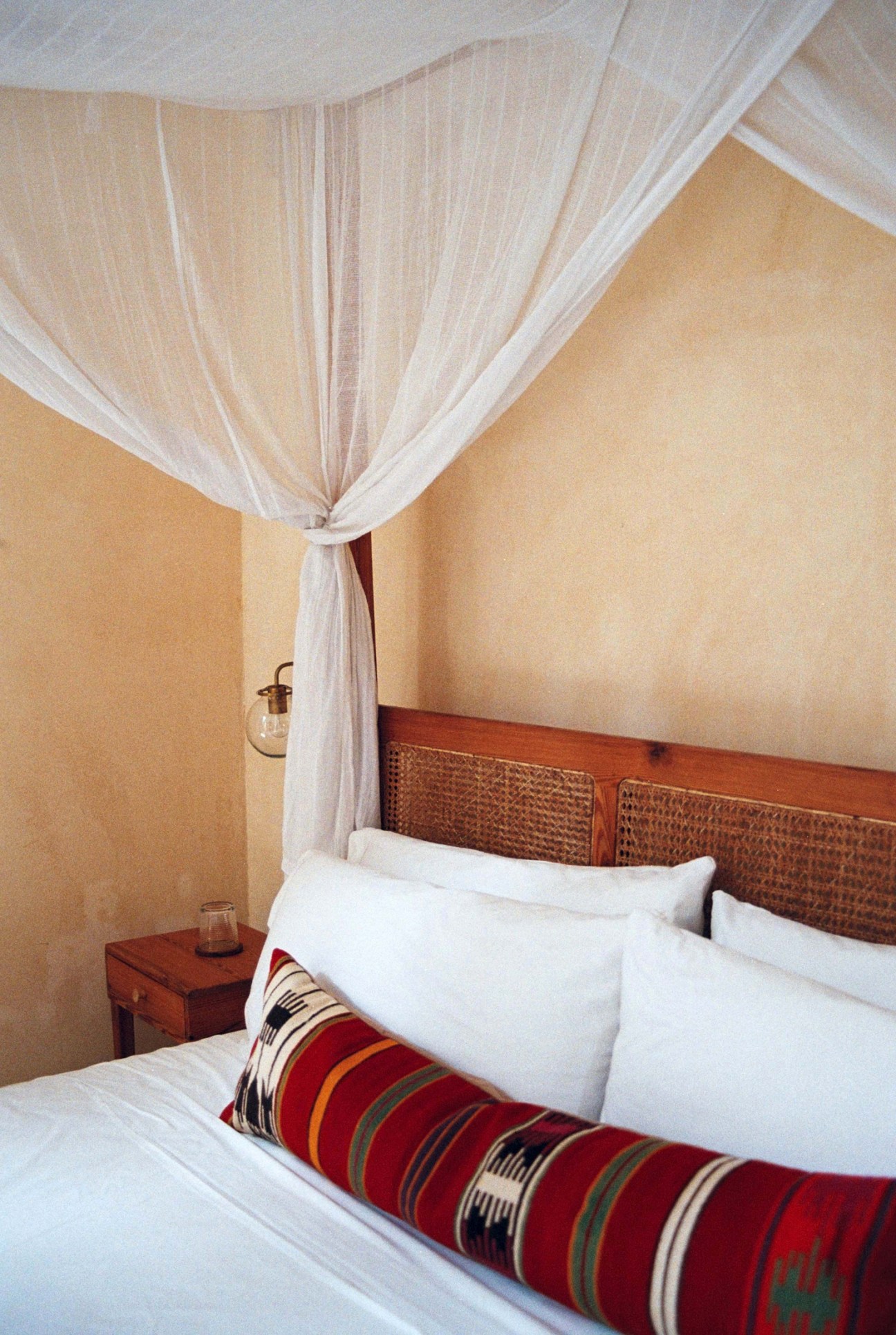 Hotel bedroom with white mosquito netting canopy over bed, striped throw pillow, and wicker headboard