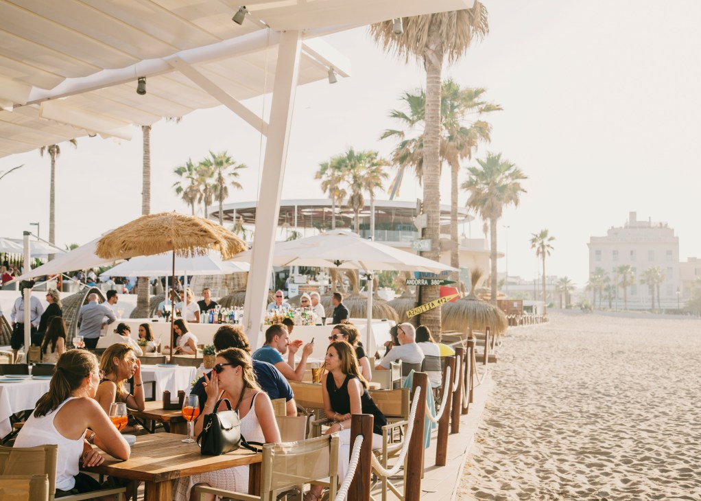 Beachgoers dining under white pergolas and umbrellas at a Valencia beachside restaurant on Patacona Beach.