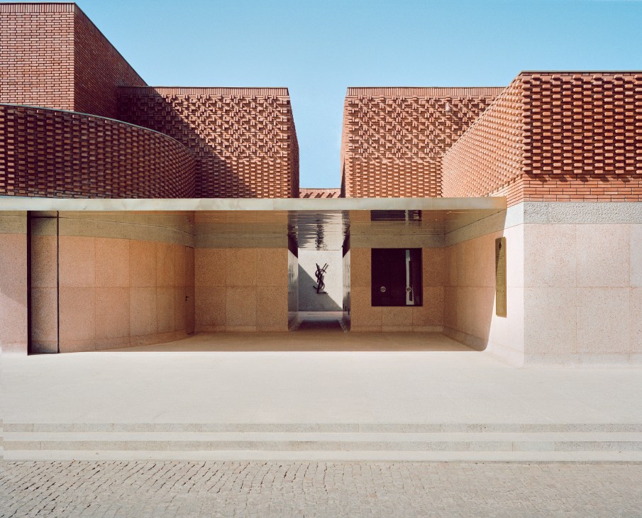 Red brick ziggurat-style museum building with patterned brickwork and a sunken courtyard entrance in Marrakech.