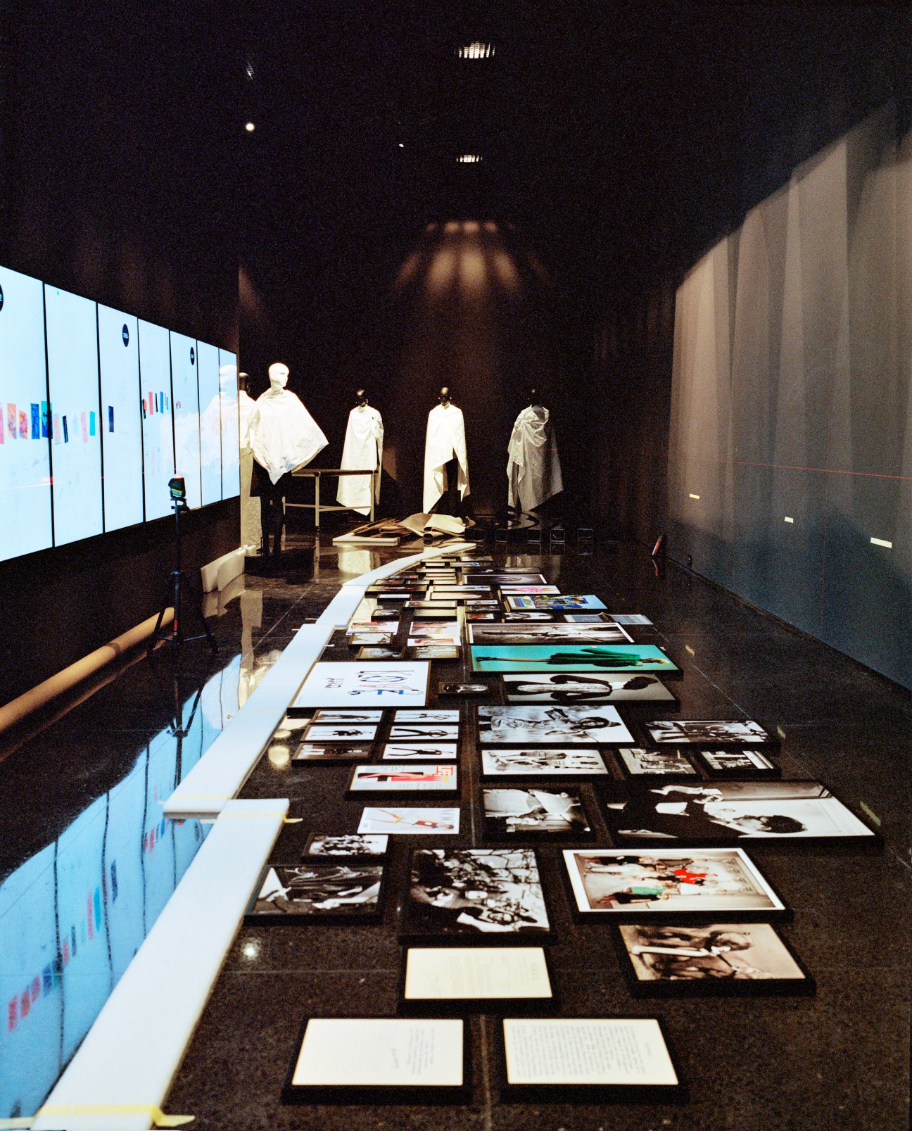 Black exhibition space displaying Yves Saint Laurent garments on mannequins and photographs on the floor.