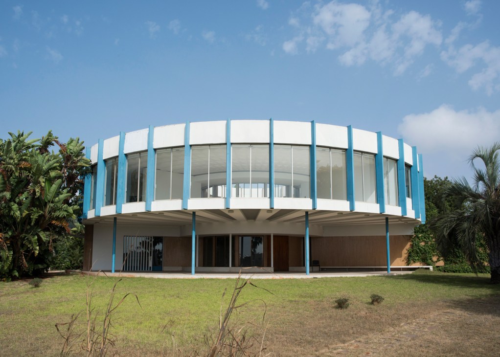 Wolfgang Ewerth's Villa Ronde, a circular modernist building with white concrete walls and blue structural columns, surrounded by palm trees.