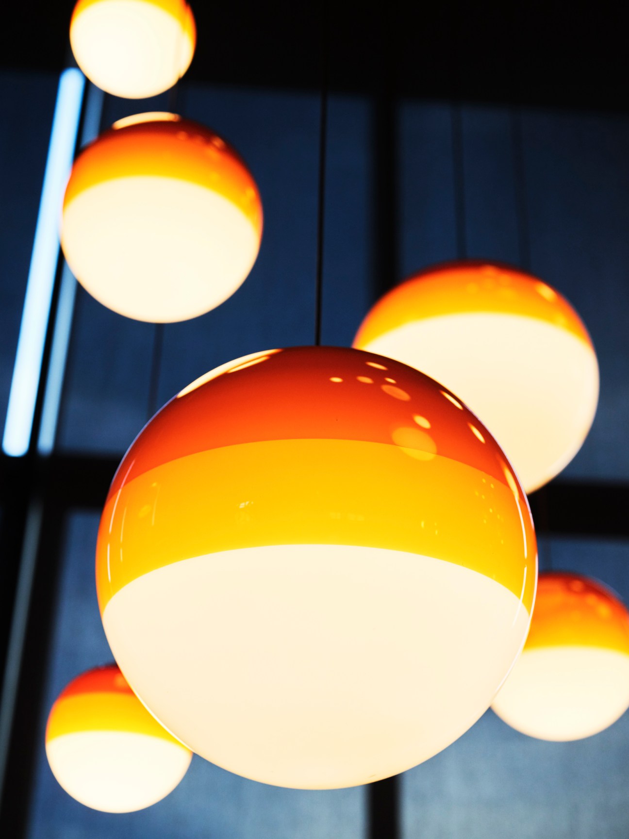 Multiple spherical pendant lights with gradient orange to cream coloring hanging at different heights