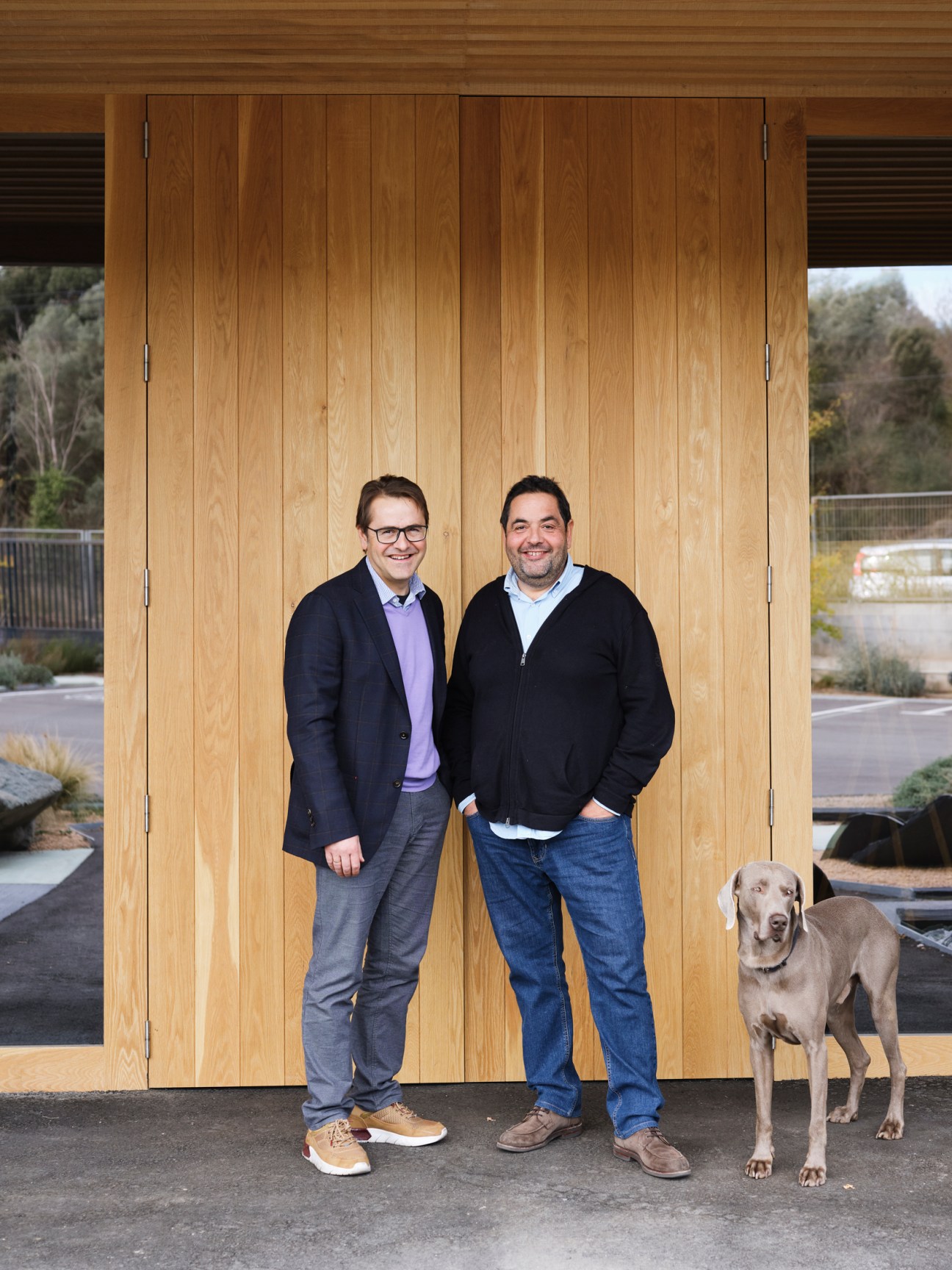 Brothers Carlos and Javier with their dog Blau standing in front of wooden doors at Marset headquarters