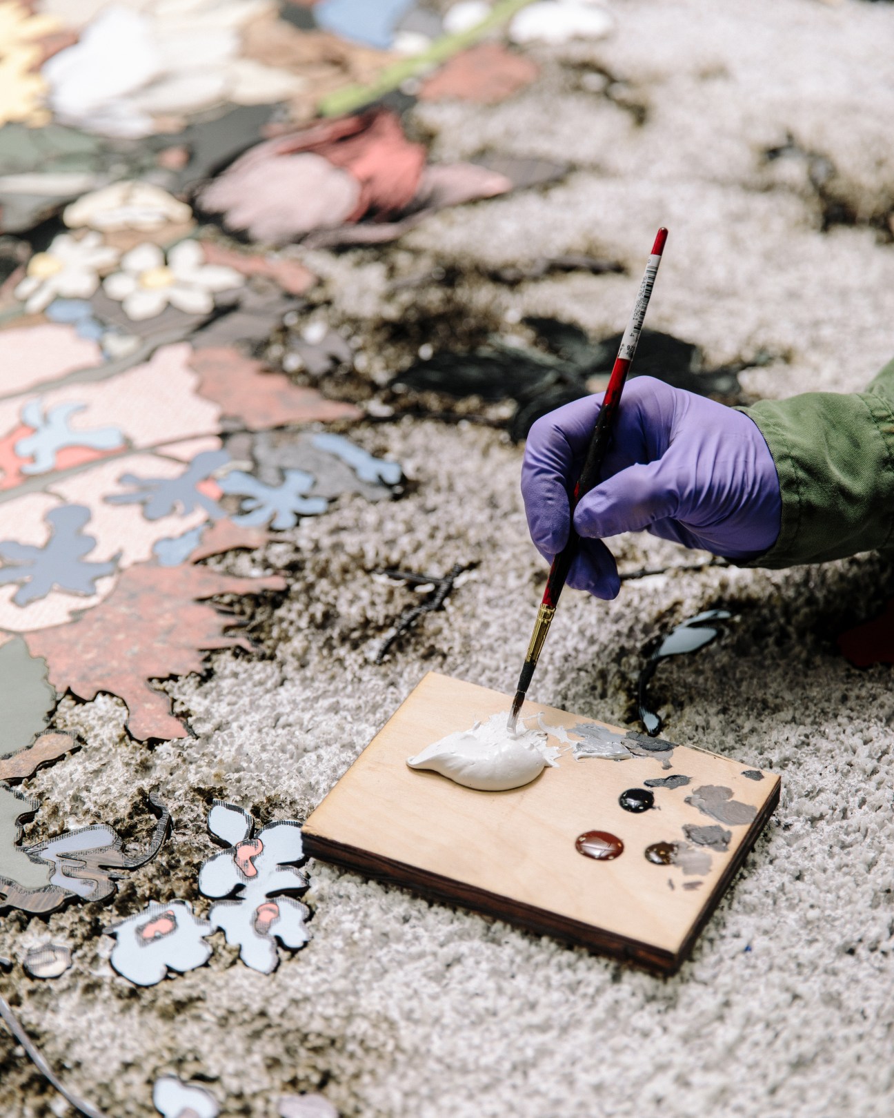 Hand in purple glove holding paintbrush above Formica artwork with flower shapes.