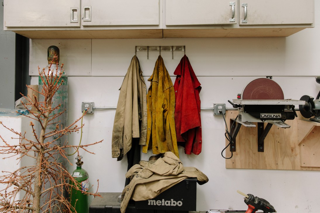 Work coats hanging on a rail in Matthew Day Jackson's studio, with tools and equipment visible.