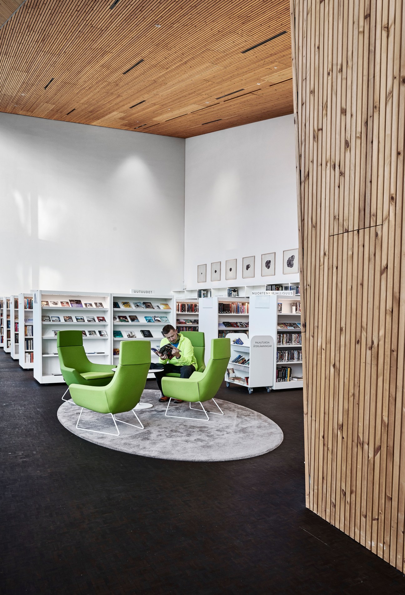 Child reading in bright green Swedese Happy chair at Maunula library with wooden wall and bookshelves