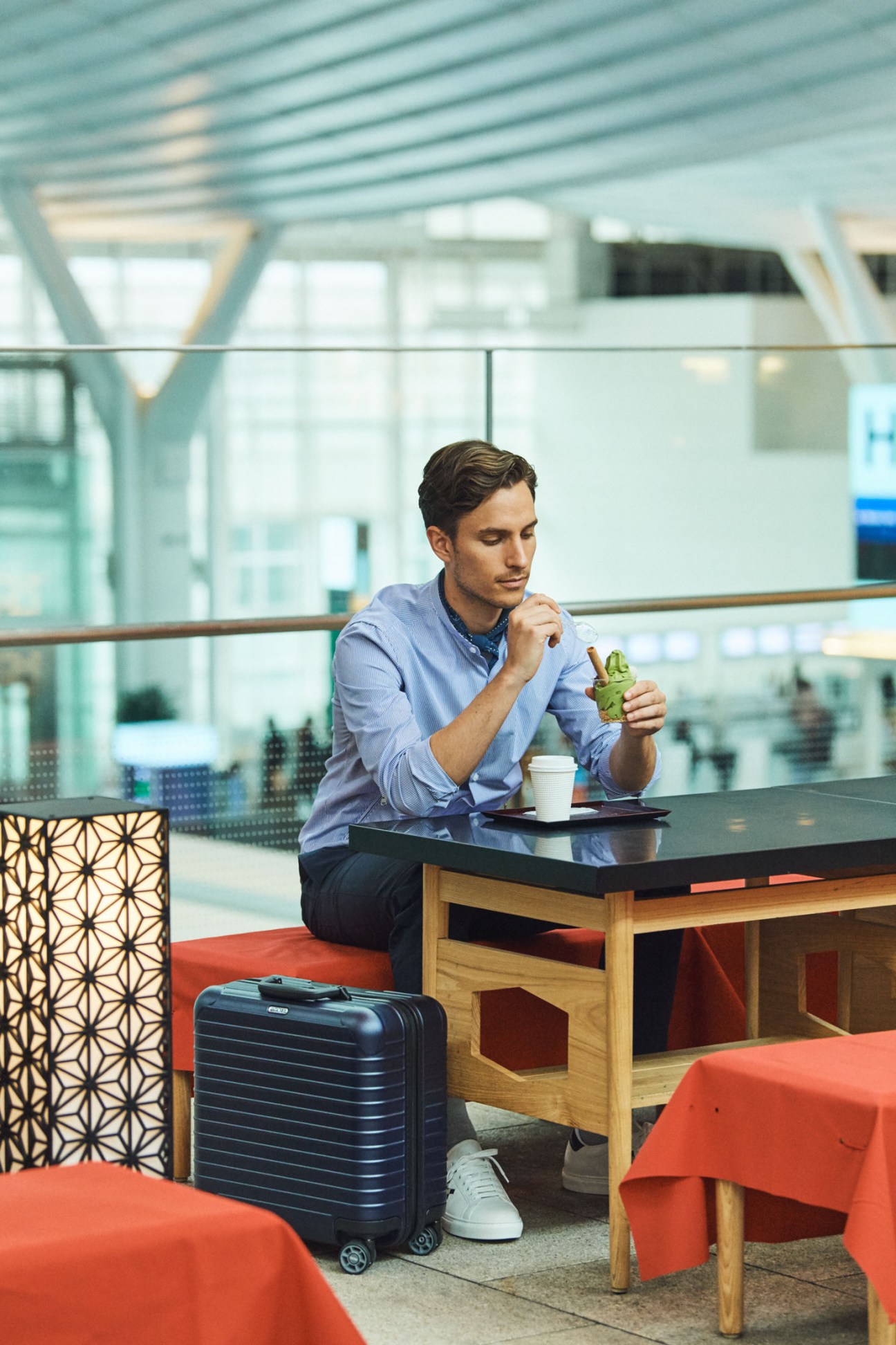 Man in light blue shirt at airport lounge with Zero Halliburton suitcase and Rimowa suitcase